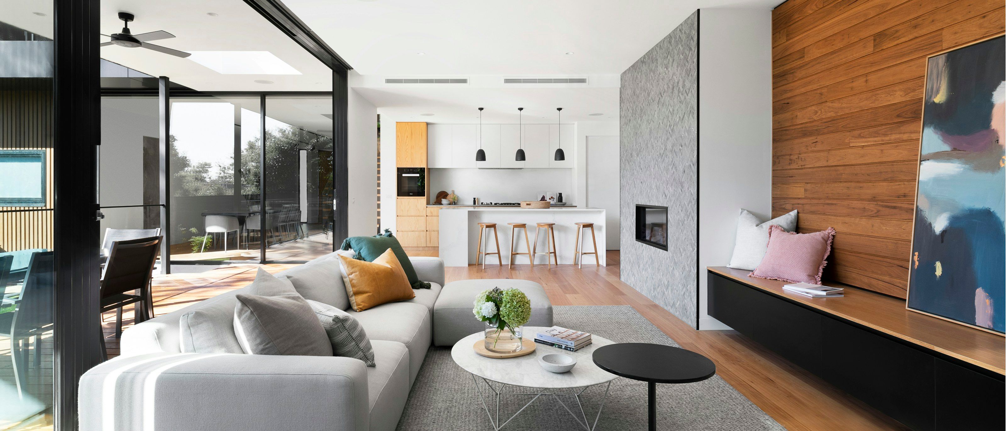 Sitting area with a grey sectional sofa facing a stone-clad fireplace, with the kitchen beyond