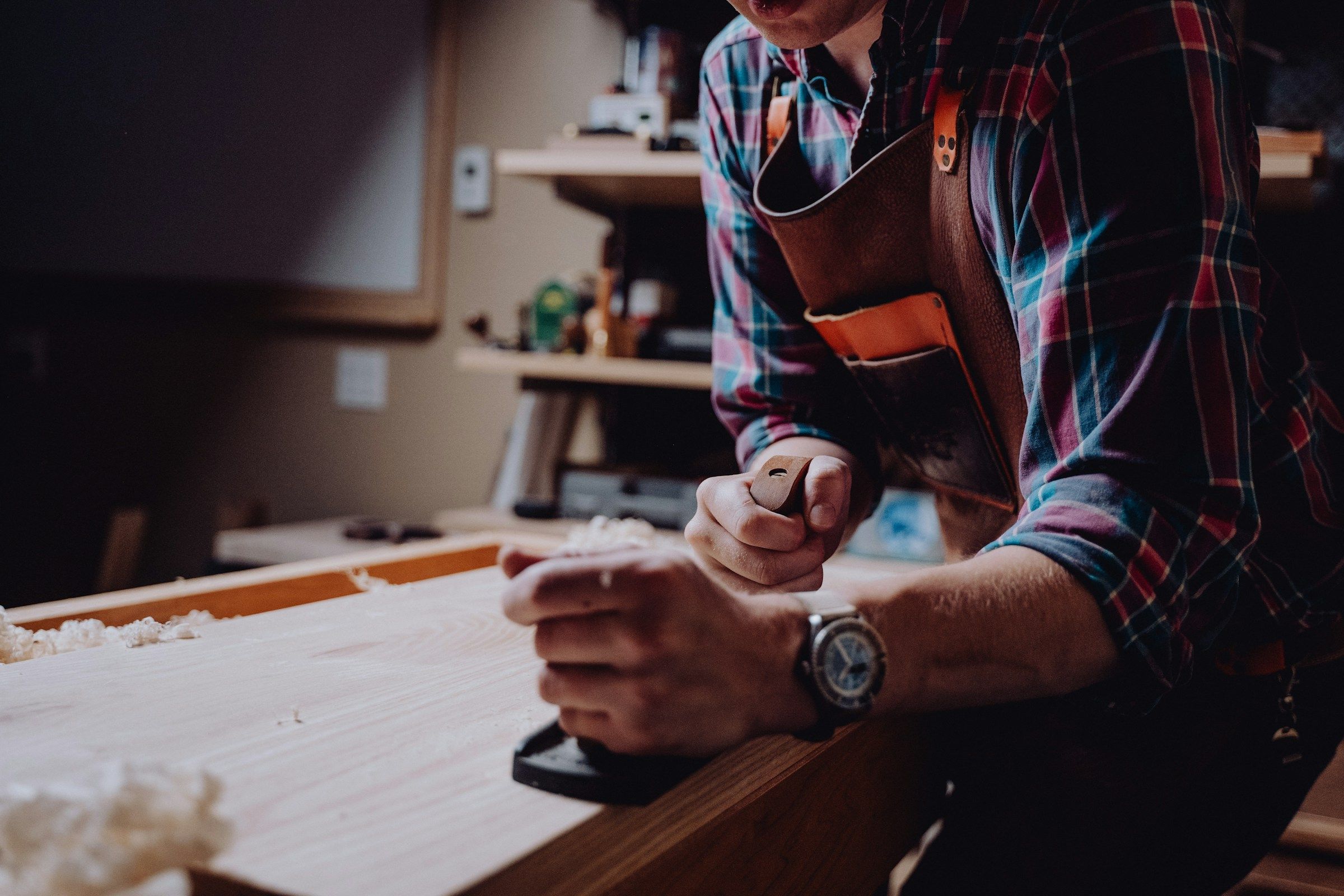 A carpenter hand-planing a length of timber on the workshop bench