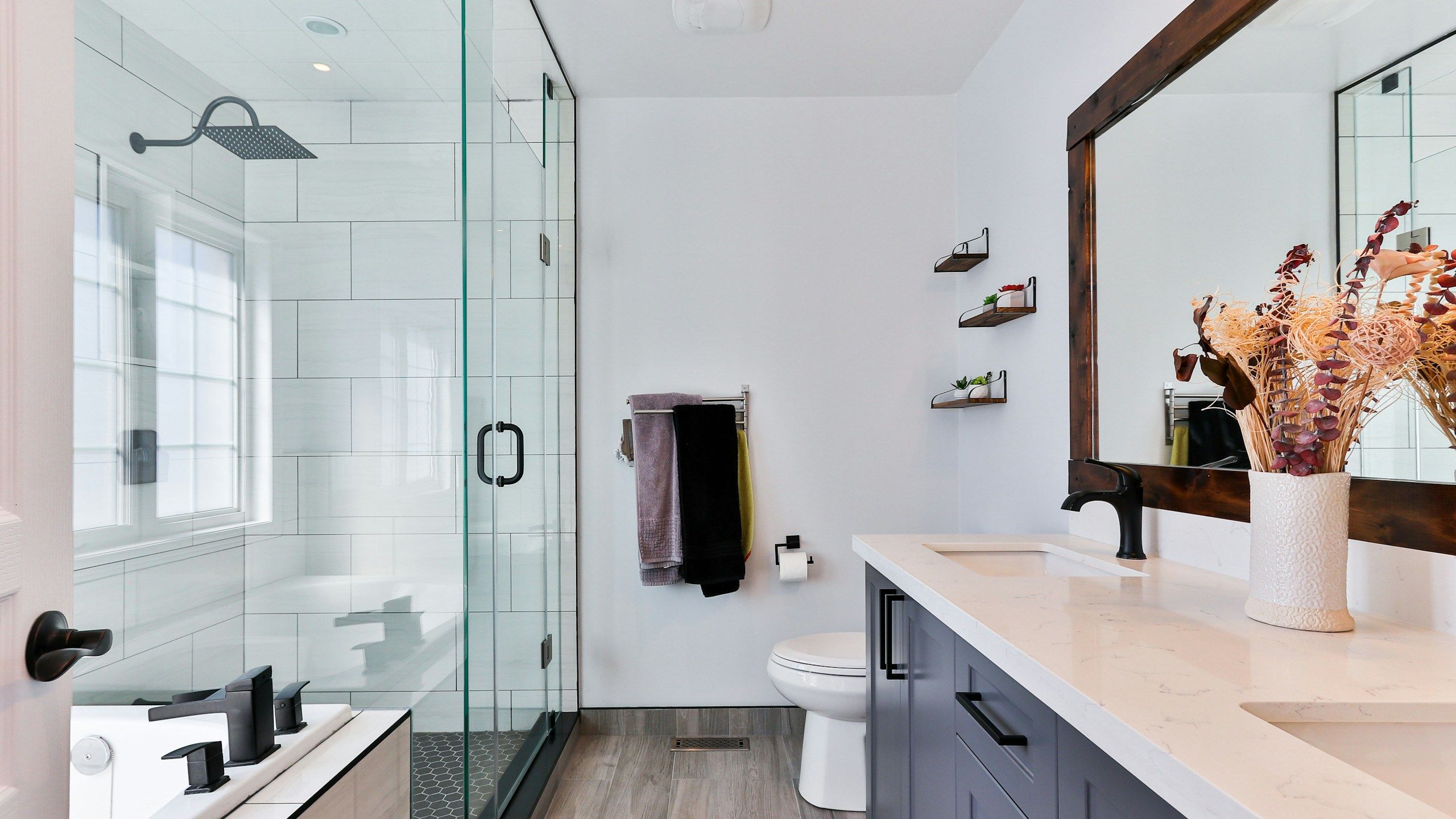 En-suite bathroom with a glass-enclosed shower, a freestanding tub and a dark timber-framed mirror over a navy double vanity