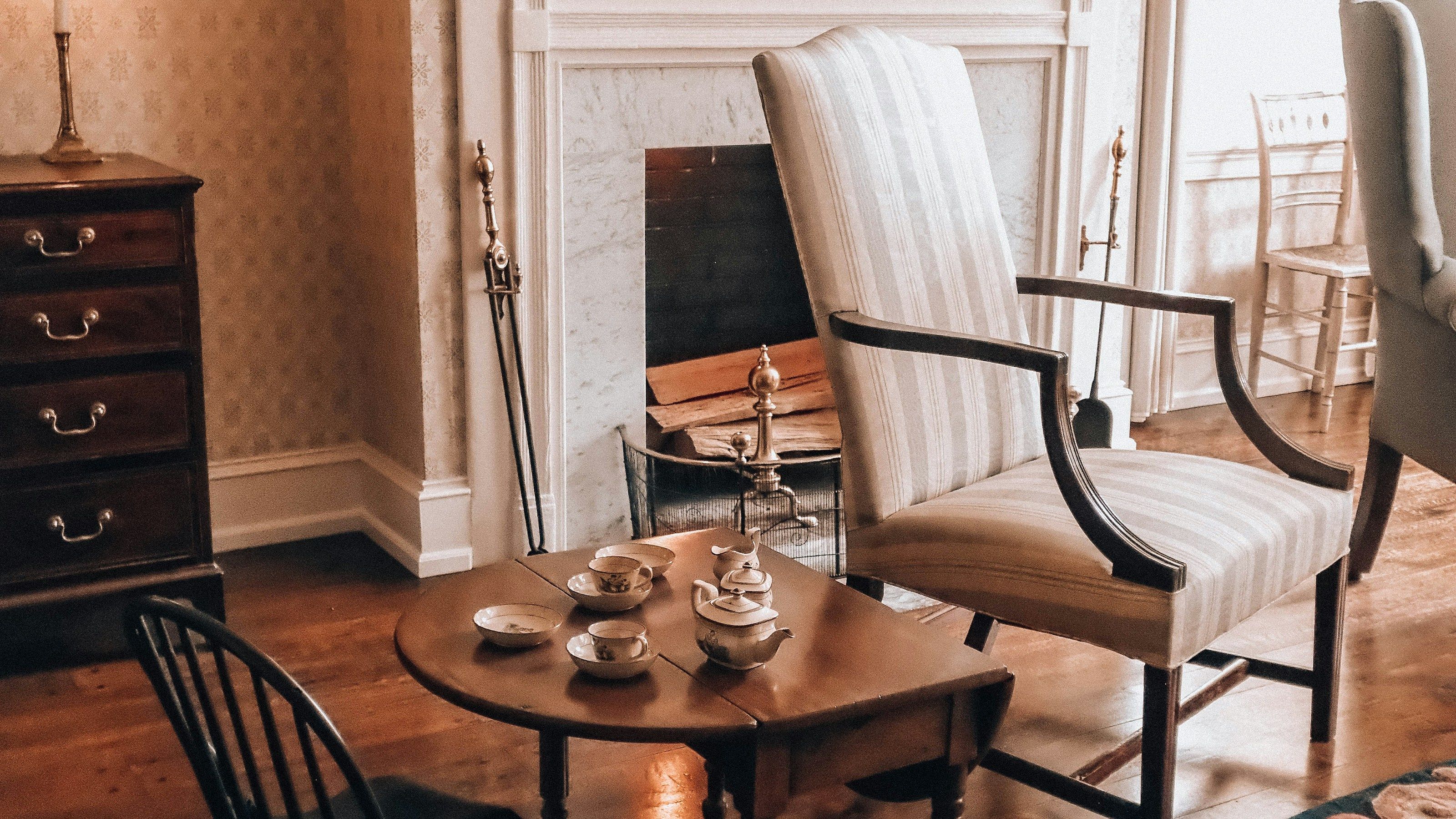 A candlelit period parlour with a fireplace, wingback chair and a tea table